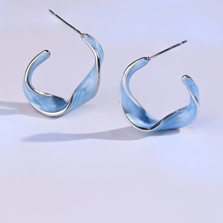 A pair of curved hoop earrings with a light blue marbled resin inlay and polished white gold edges and posts, displayed on a clean light gray background.