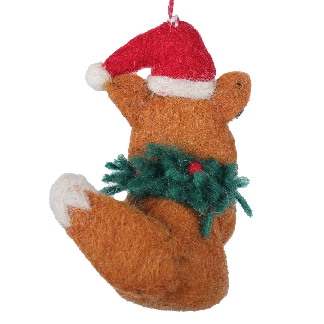 Felted fox ornament wearing a Santa hat and holding a sprig of holly on a white background