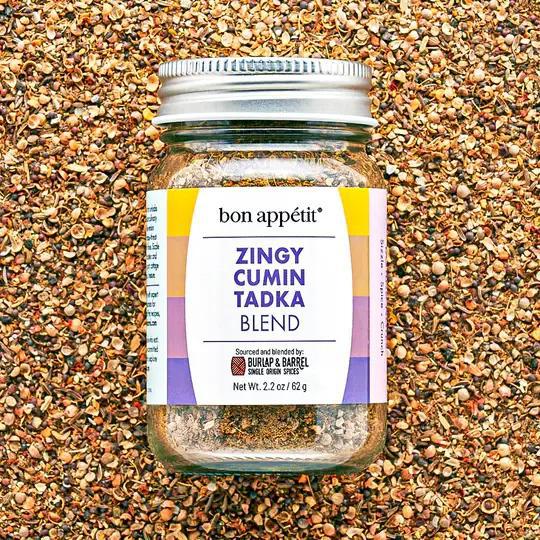 Jar of Zingy Cumin Tadka Blend on a textured spice background