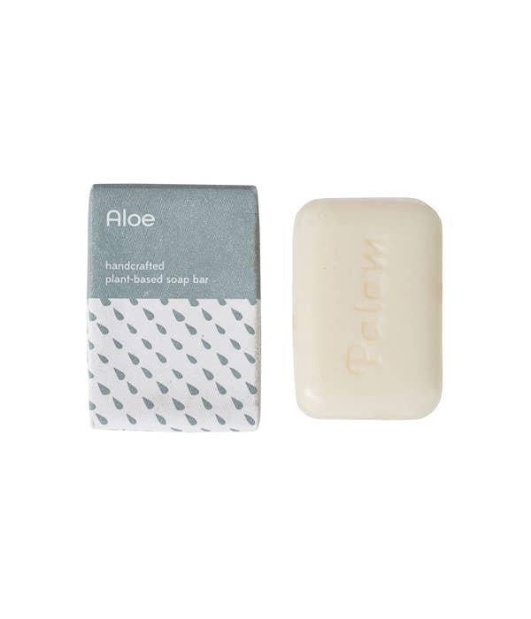 A bar of soap next to its packaging, which has 'Aloe' and 'Handmade in India' printed on it. The packaging is primarily white with a grey pattern 