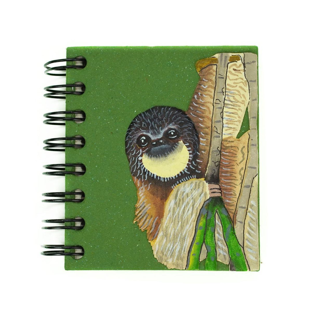 A small spiral notebook with a green cover featuring a hand-drawn illustration of a sloth.