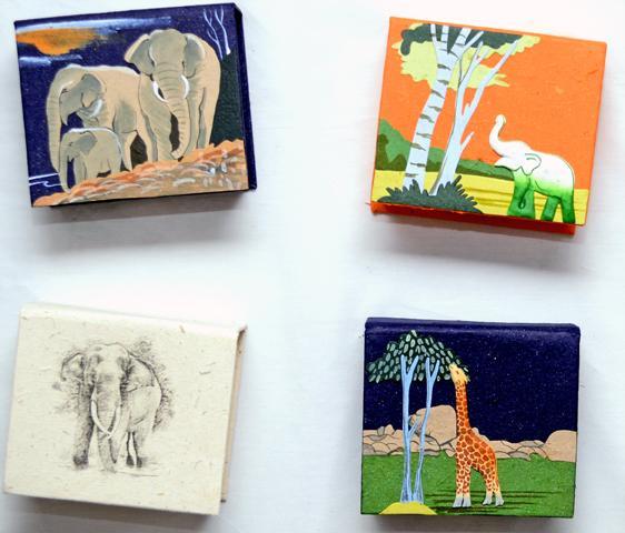 Several square note boxes with various animal designs, including an elephant, a giraffe, a lion, and a crocodile, made of recycled paper with hand-painted illustrations.