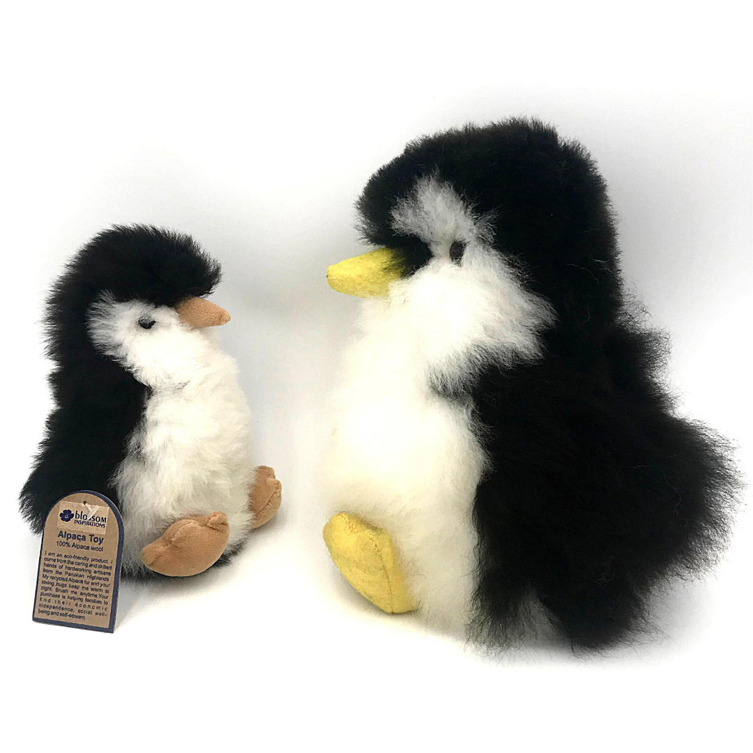 Two plush penguin toys made from alpaca fur. One is significantly larger than the other, both with black and white fur, yellow beaks and feet, and a tag indicating the product is handmade in Peru.