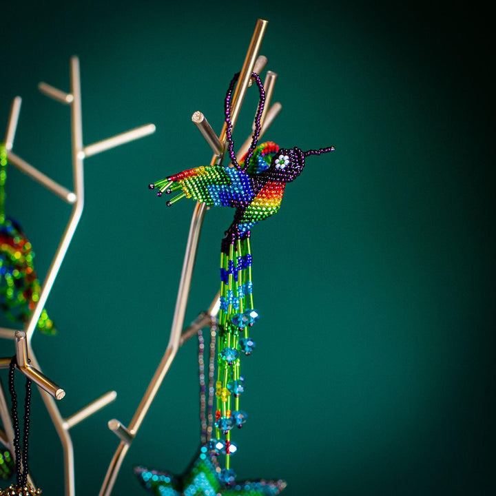 A colorful beaded hummingbird ornament hanging from a loop, with a design that includes multiple beads in various colors.