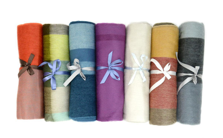 A selection of folded brushed acrylic lap blankets in various solid colors, each adorned with a decorative ribbon.