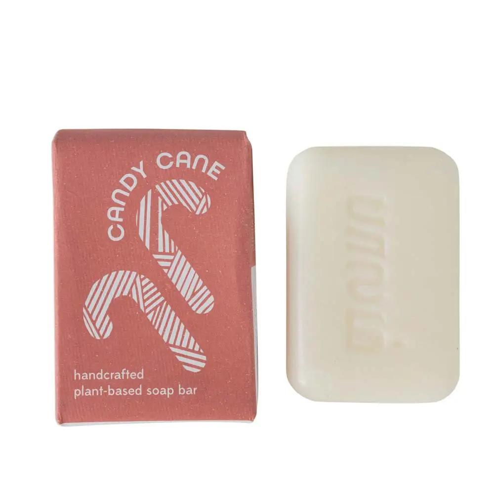 A bar of handcrafted soap with a candy cane design on the packaging, alongside its pink box packaging labeled 'Candy Cane Soap, Handmade Plant-Based Soap Bar'.
