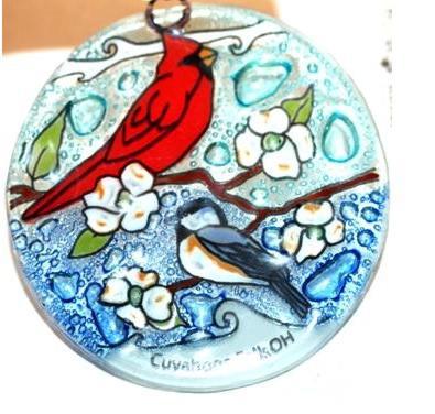 Handmade glass ornament of a cardinal and chickadee sitting on branches with white blossoms. 