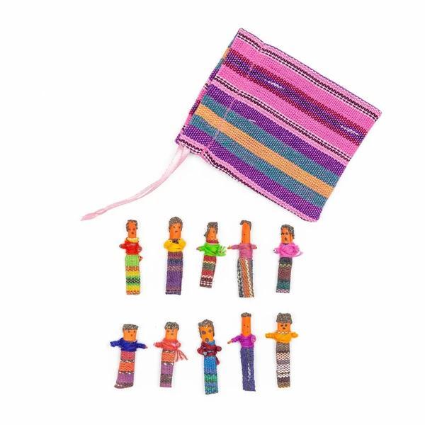 A set of colorful worry dolls in various poses alongside a striped purple, pink, and orange bag.