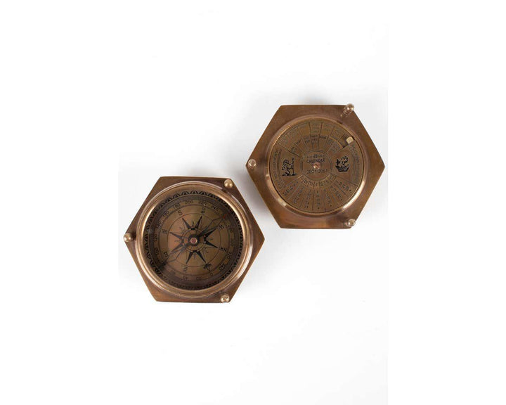 A brass compass-shaped calendar with a glass face on one side and a 40-year calendar on the other, placed on a white background.