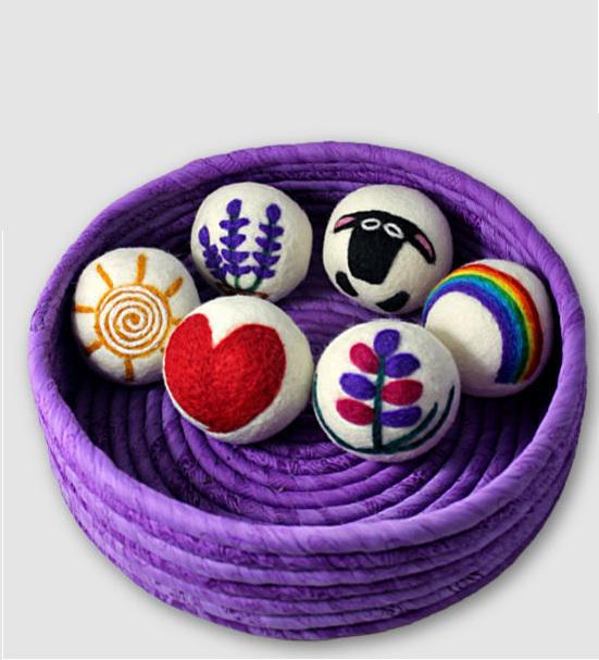 A basket containing multiple multicolored felt dryer balls with various designs, placed on a purple surface.