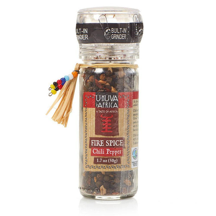 A clear glass spice grinder bottle with a label reading 'Fire Spice Chili Pepper', with a decorative tassel on the cap.