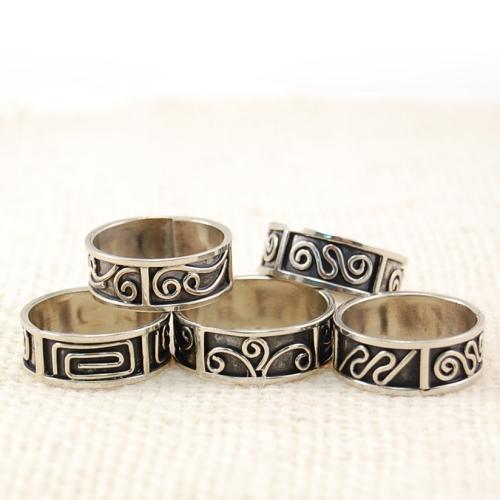 A collection of silver rings with intricate geometric designs, displayed on a textured background.