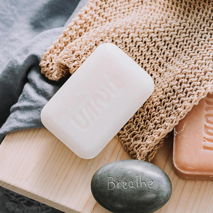 Hand-crafted lavender scented soap on shower scrubber with charcoal rock that says 'Breathe'. 
