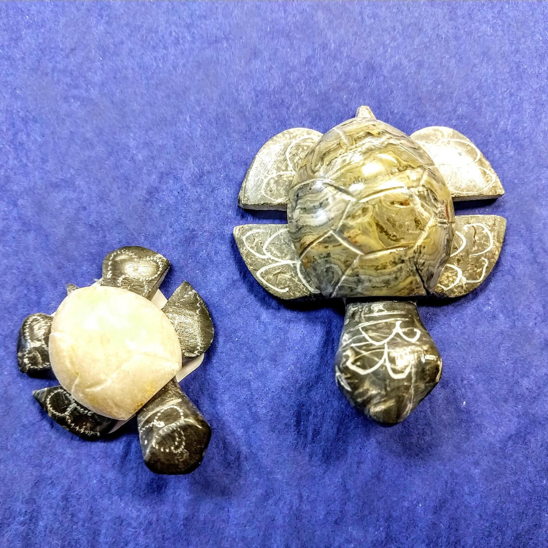 Two turtle-shaped sculptures made of black marble and onyx stone, with one larger than the other, placed on a blue background.