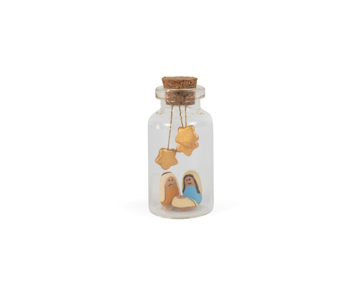 A small decorative nativity scene inside a glass bottle with a cork stopper, featuring ceramic figures of Mary, Joseph, and baby Jesus, and three hanging stars.
