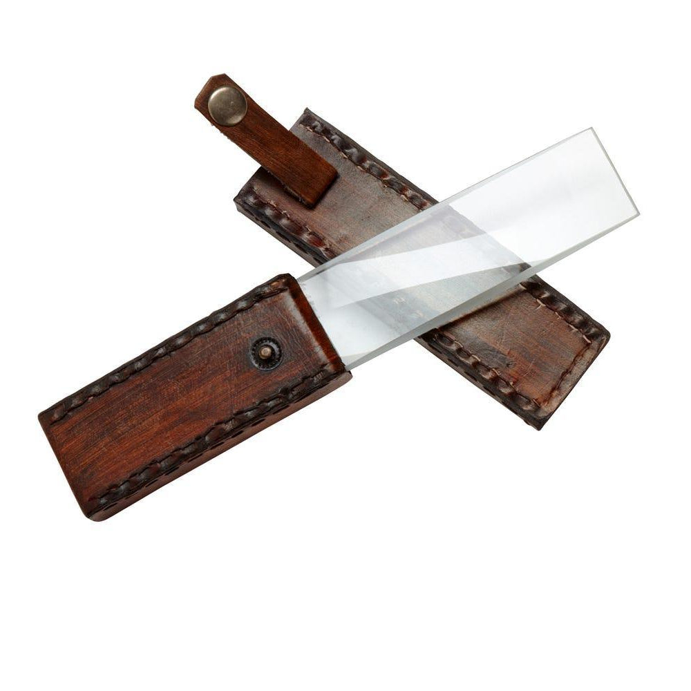 A handcrafted leather handle and sheath with a magnifying glass lying across it, isolated on a white background.