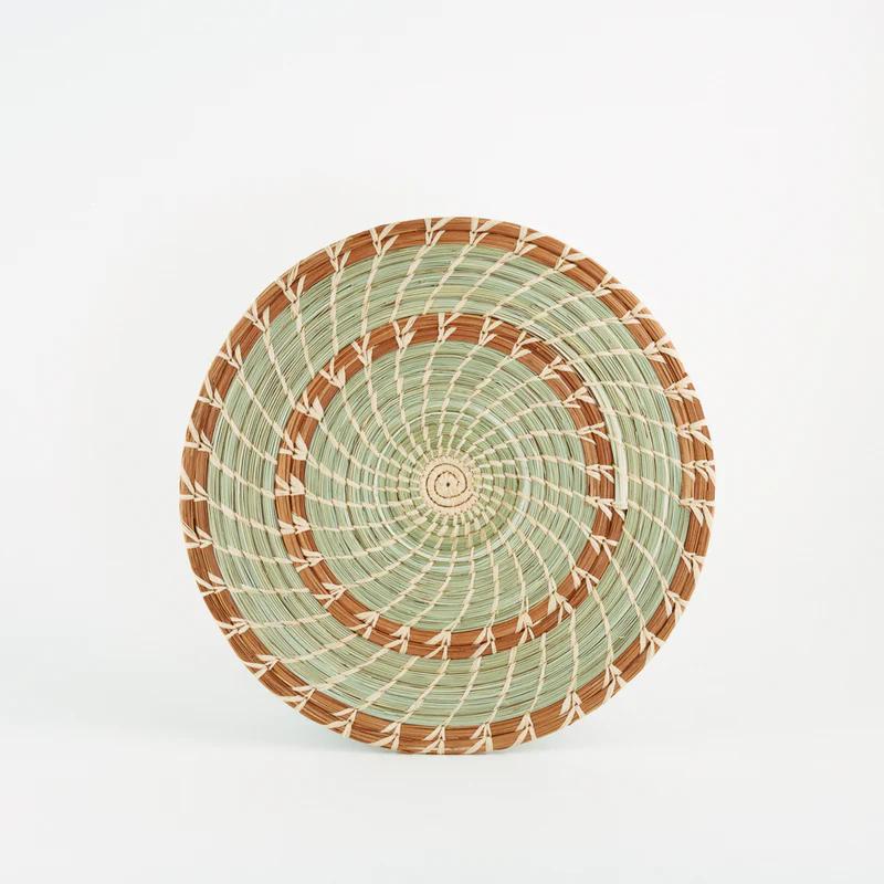 Handmade woven pine and grass trivet with brown and green spirals on a white background.