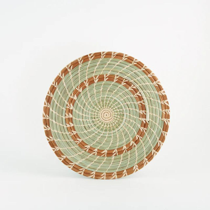 Handmade woven pine and grass trivet with brown and green spirals on a white background.
