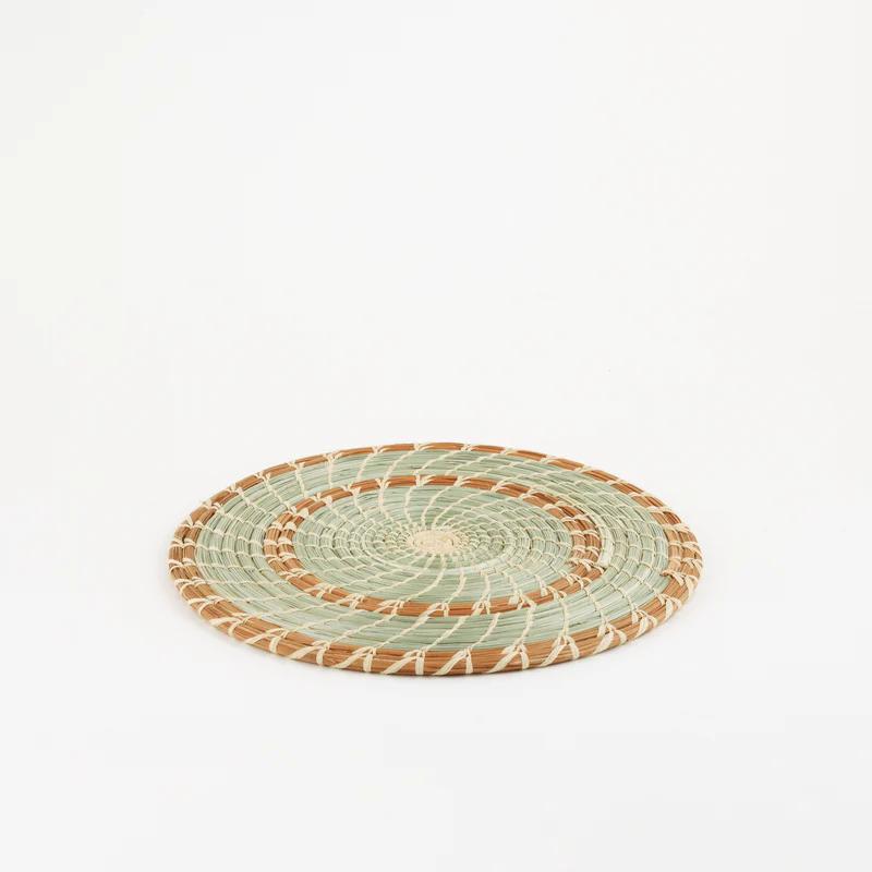Handmade woven pine and grass trivet with brown and green spirals on a white background.