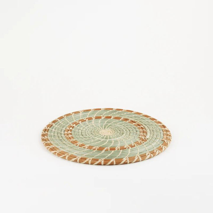Handmade woven pine and grass trivet with brown and green spirals on a white background.