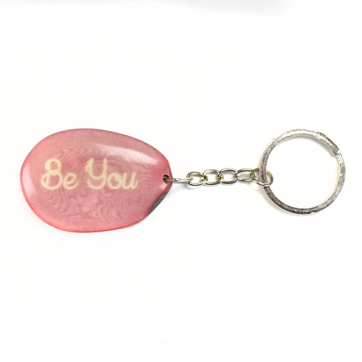 a pink tagua keychain with the words 'be you' engraved