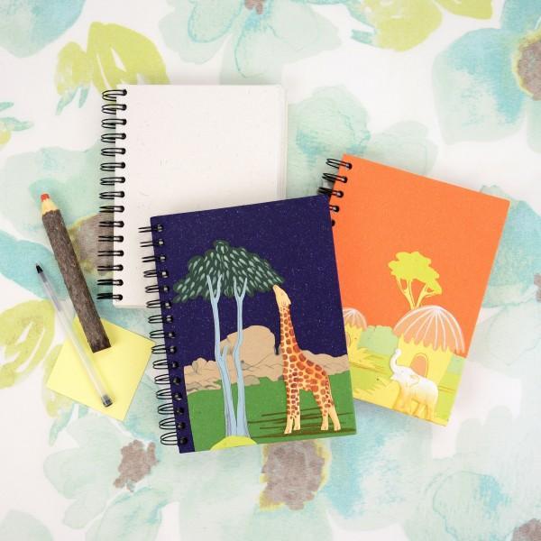 A elephant poo spiral notebook and a spiral notepad with colorful elephant-themed illustrations on the covers, displayed on a patterned background.