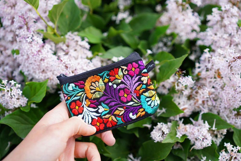 a person holding a colorful coin purse with lilacs in the background