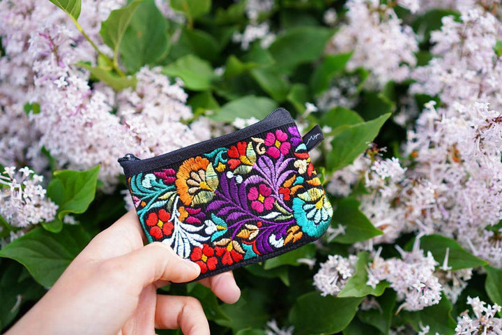 a person holding a colorful coin purse with lilacs in the background